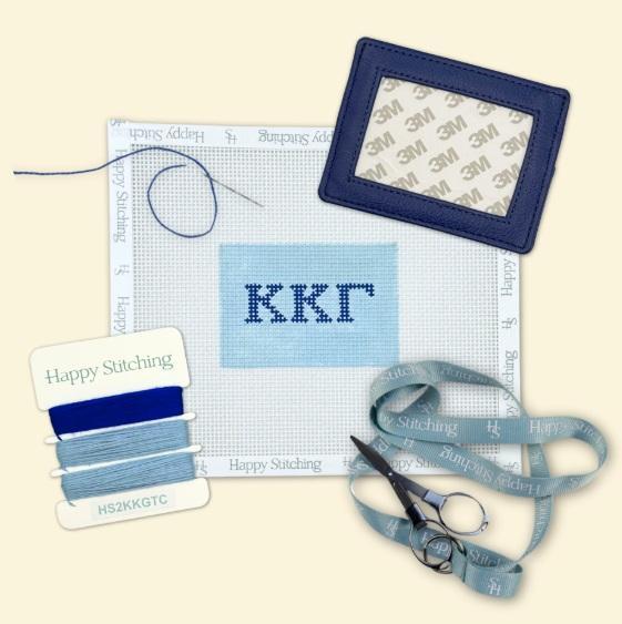 Needlepoint card wallet kit with blue stitched panel, navy frame, thread and scissors
