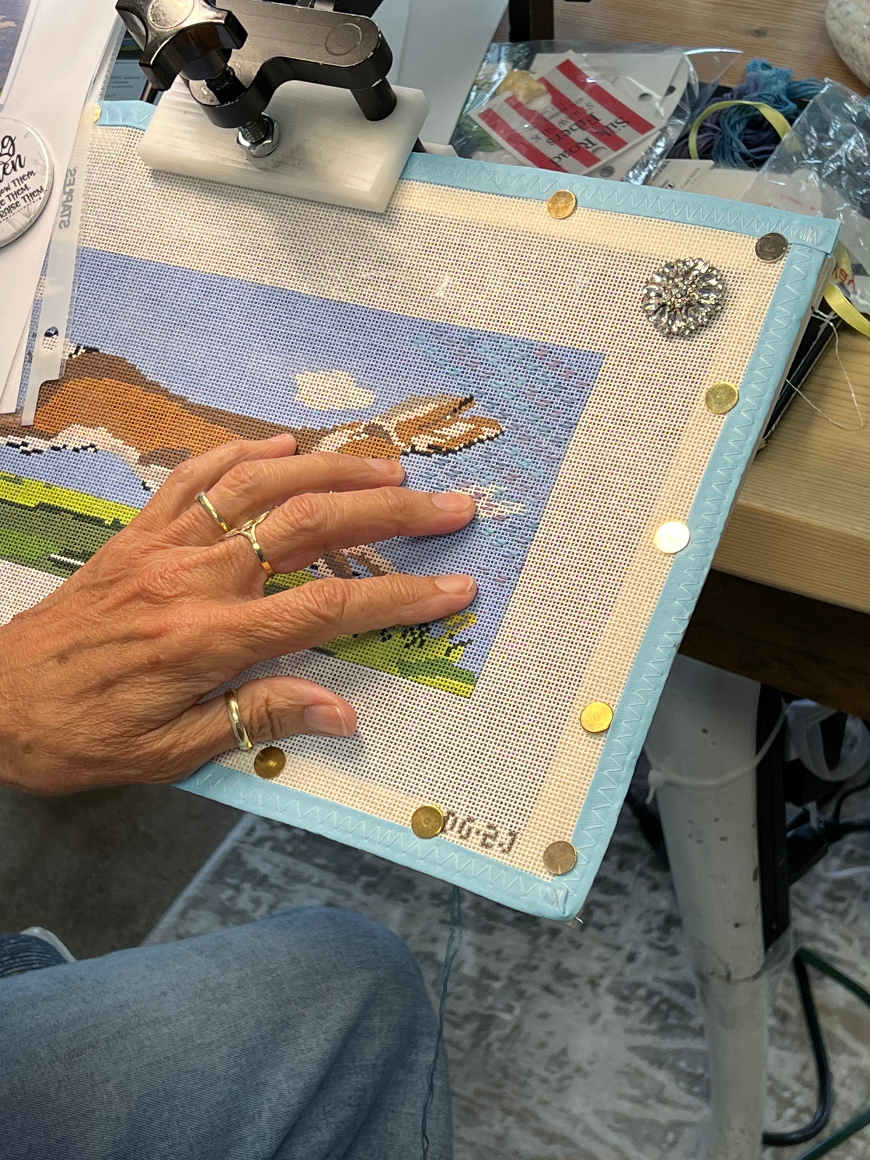 Light blue needlepoint canvas with colorful stitched motif under a hand