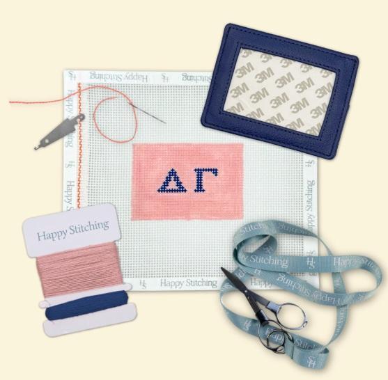 Needlepoint card wallet kit with pink stitched panel, blue frame, thread and scissors