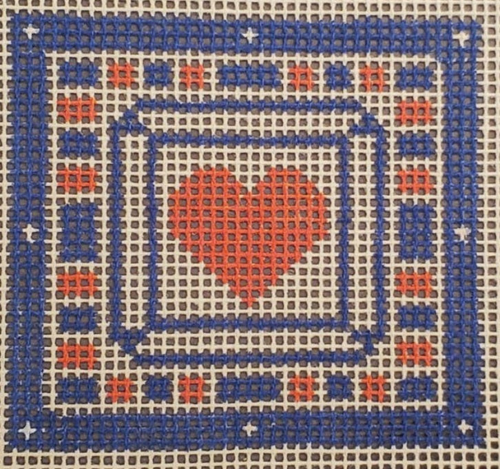 Blue framed cross-stitch heart on white-and-orange grid cloth