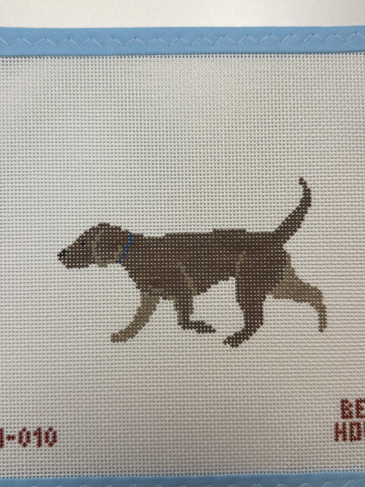 Embroidered dark brown dog standing in side view with raised tail