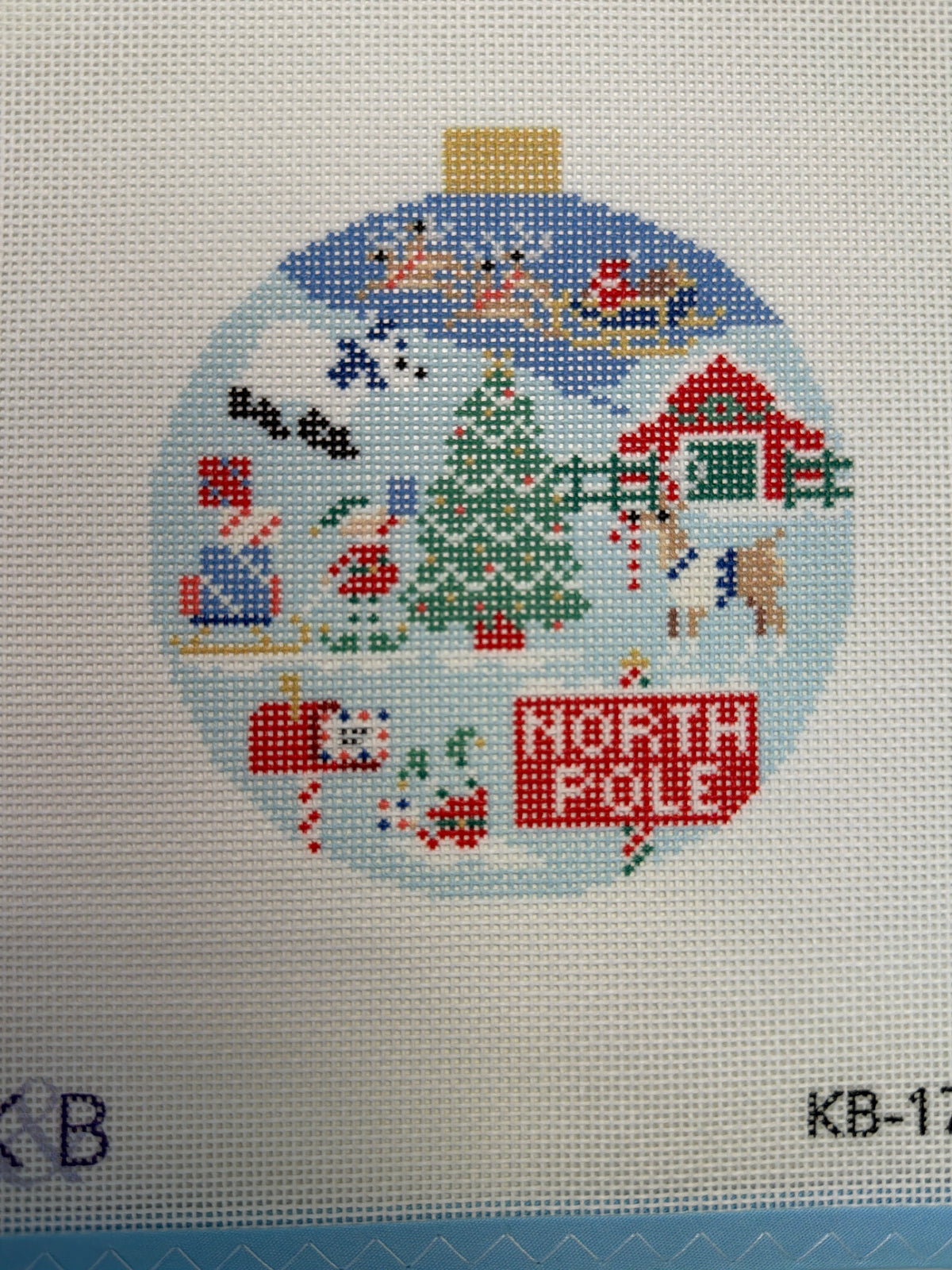 Round North Pole themed ornament with winter scenes, house, trees, and penguin figures