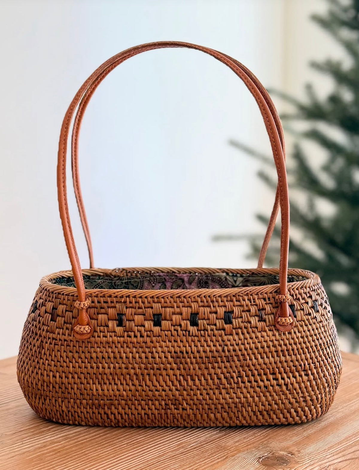Rattan handbag with rounded woven top, tan handles, dark purple patterned interior lining