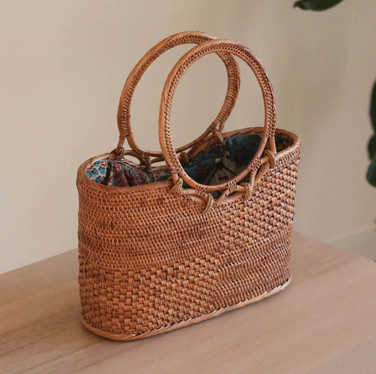 Rattan tote bag with woven body, tall oval handles, blue floral fabric lining