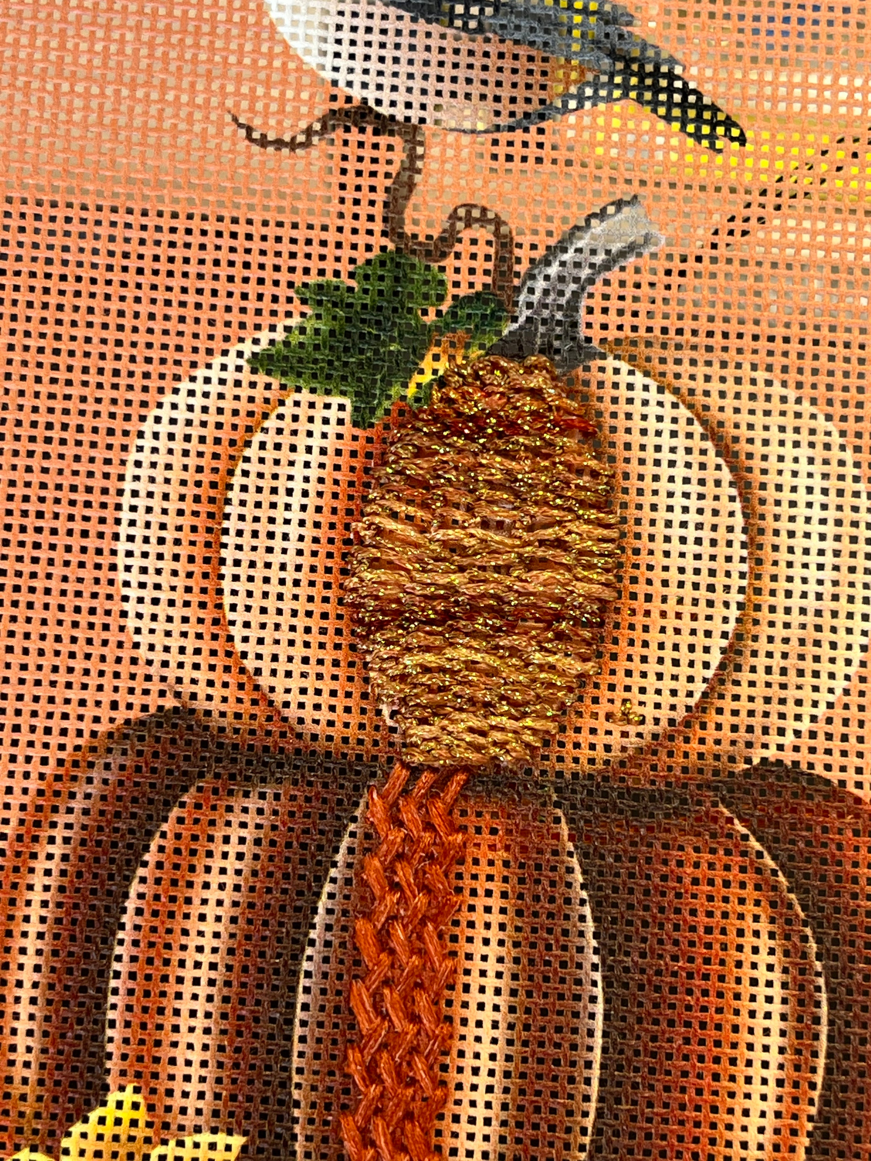 Gold and orange stitched pineapple motif with green accents on needlepoint canvas