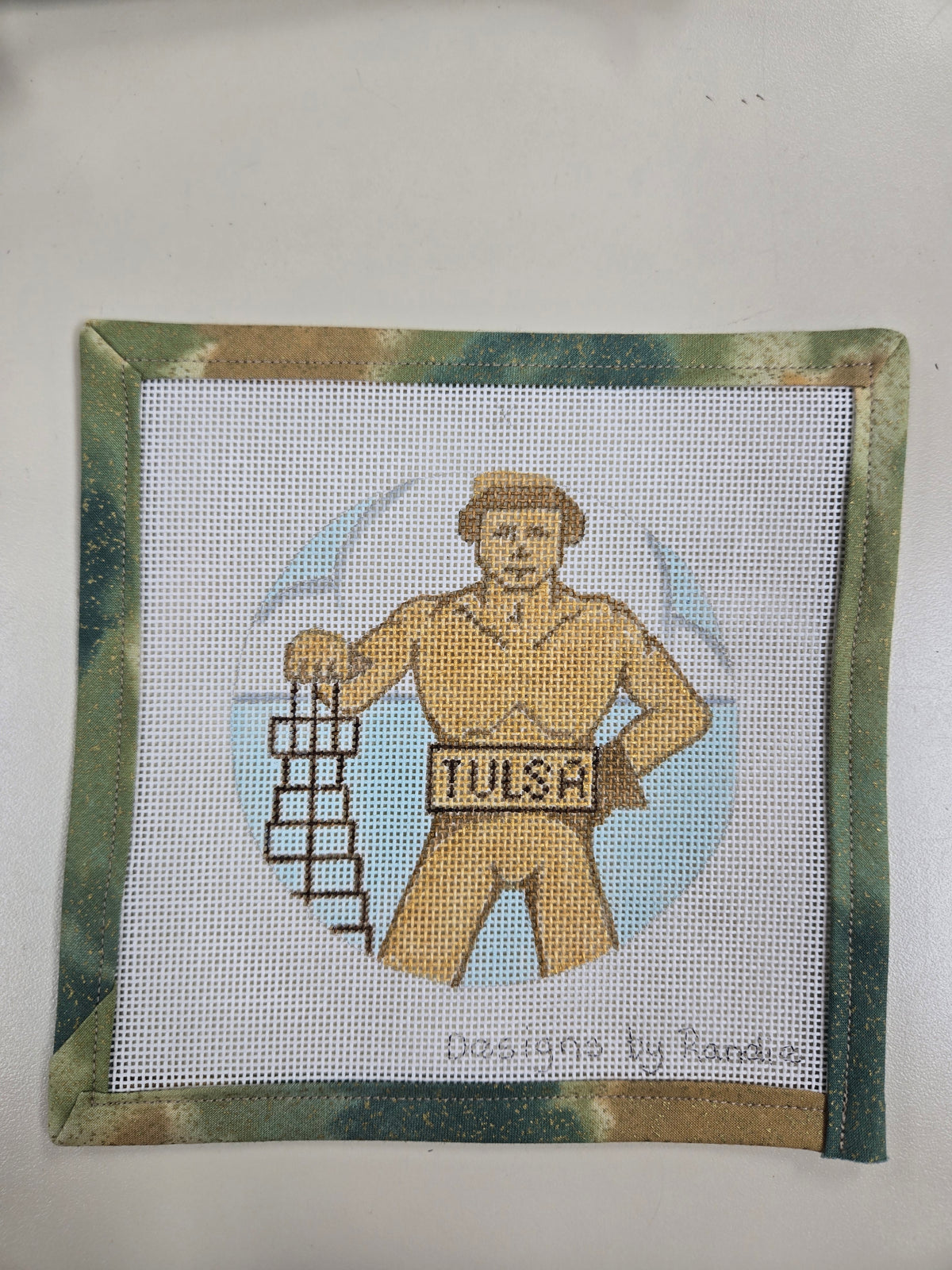 Golden Driller needlepoint square featuring a gold-colored oil worker