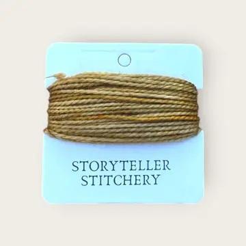 Hand-dyed embroidery thread spool in tan with subtle flecks on a card backing.