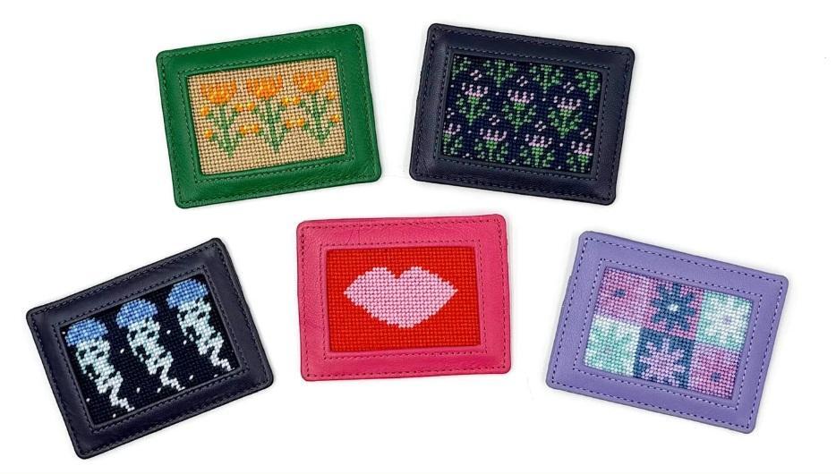Needlepoint card wallets set with five stitched designs in green, black, pink, and purple frames