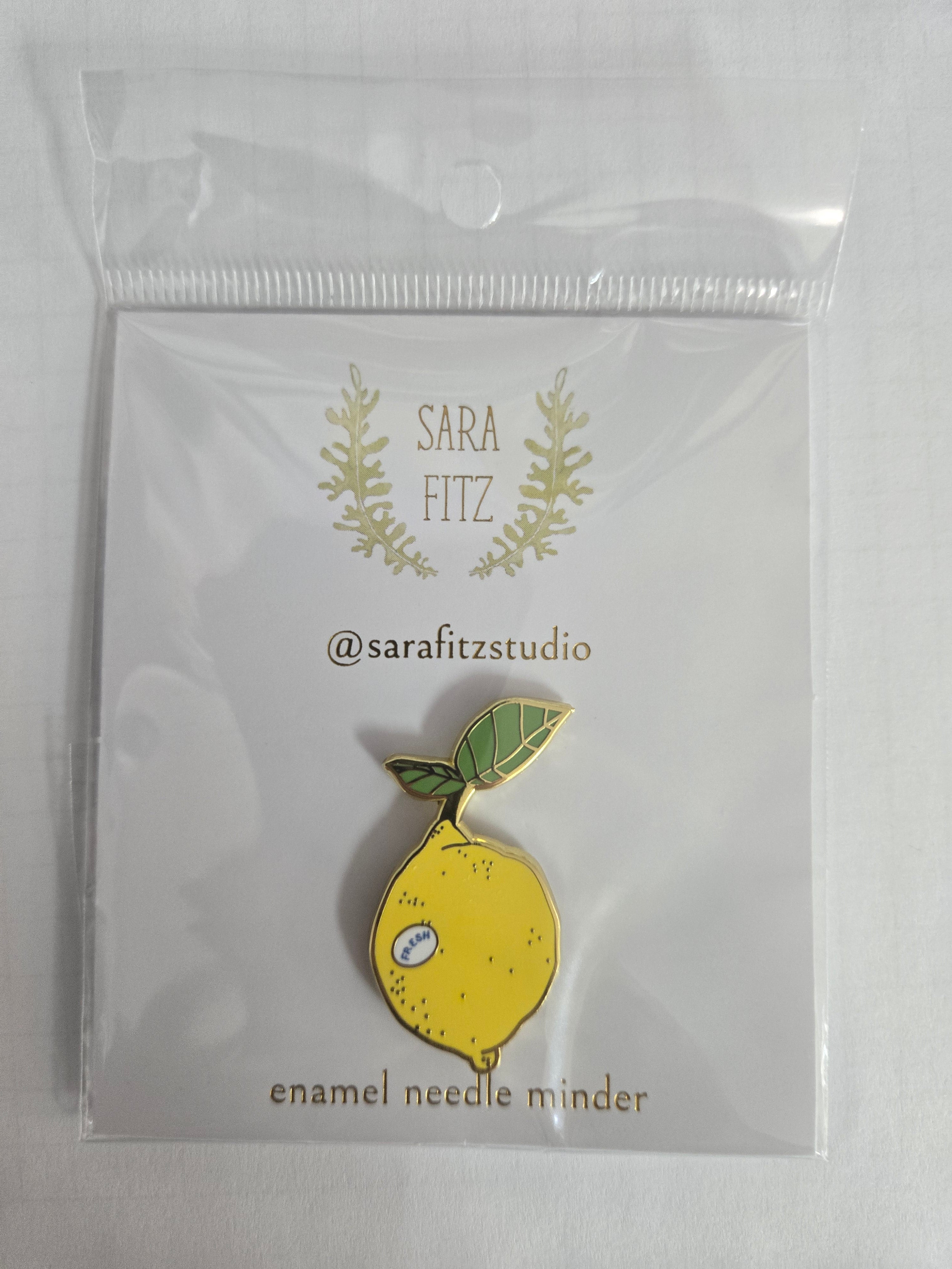 Lemon enamel needle minder with green leaf accents, Sara Fitz studio logo