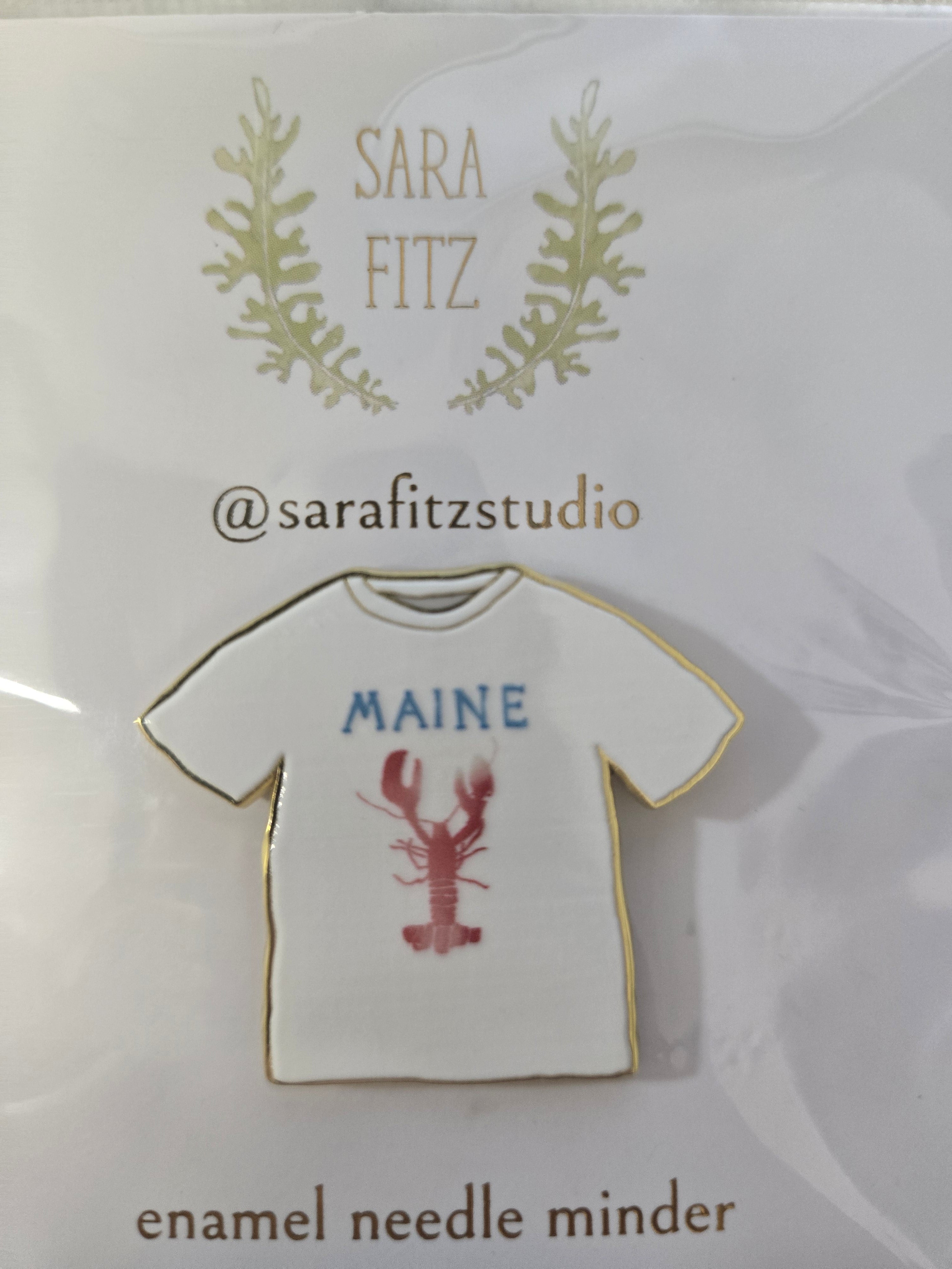 Enamel needle minder shaped like a white tee with "MAINE" and a red lobster