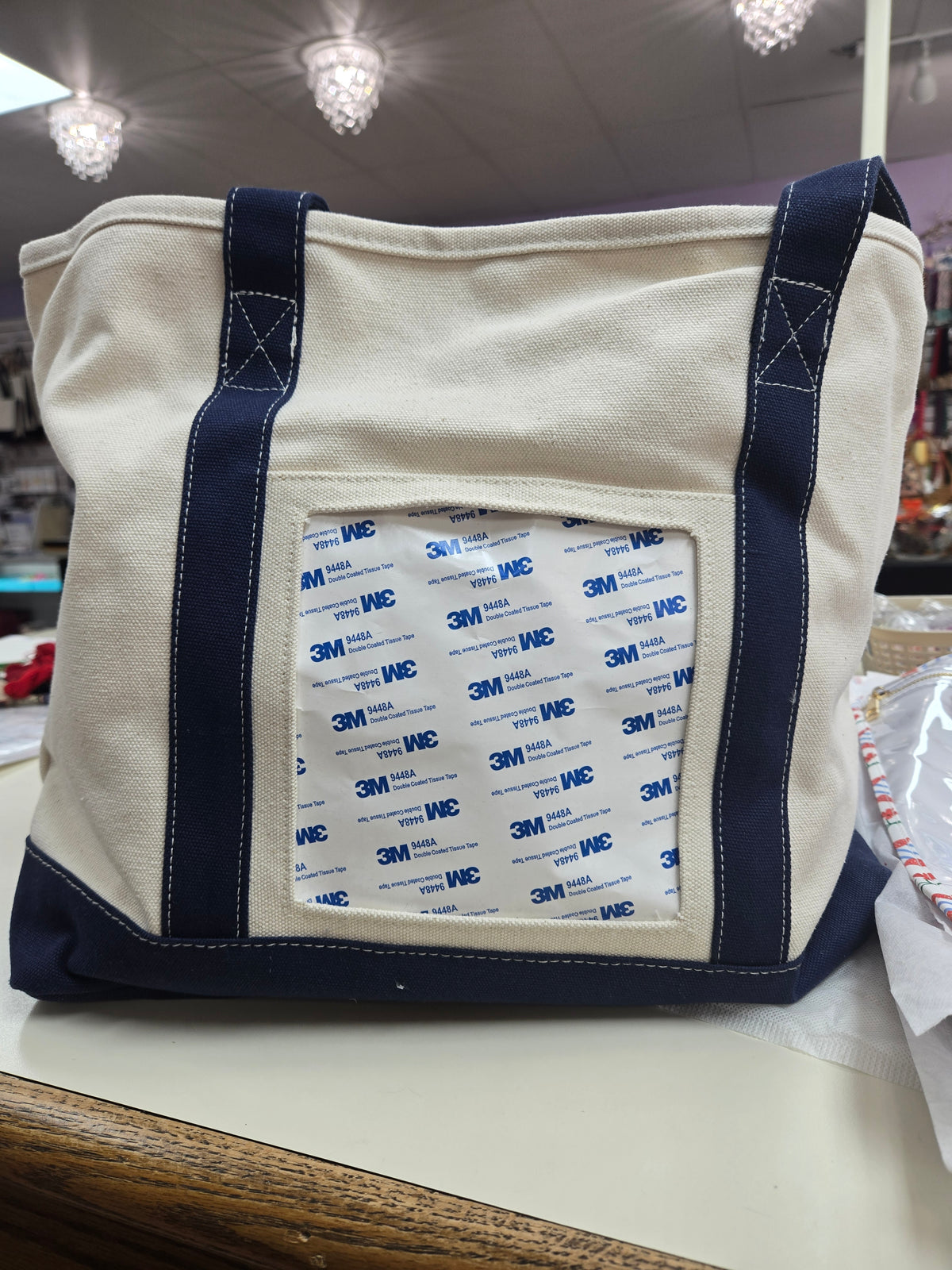 Canvas tote bag with navy handles and trim, front clear pocket with 3M labels